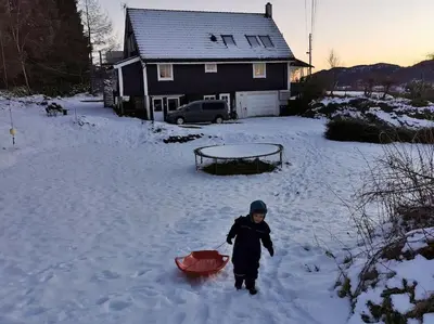 a young boy standing in the snow with a red sled at Small Basement Apartment Private Entrance Nice View in Fitjar