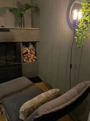 a living room with a fireplace and a chair and a lamp at Skogro ved Norefjell in Noresund