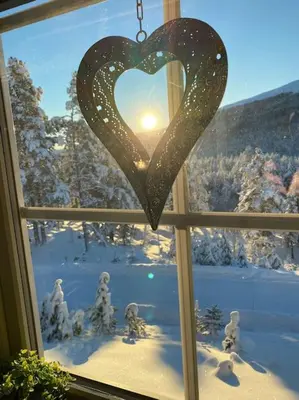a heart ornament hanging from a window with a winter view at Cozy apartment near Besseggen with a private sauna in Randsverk