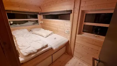a small bed in a wooden room with two windows at Heimstølen - Cabin at Sørbølfjell in Flå
