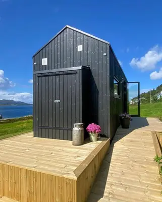 a black building on a wooden deck with flowers at Kråen Gard in Larsnes