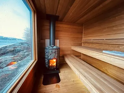 a sauna with a fireplace in a wooden room with a window at Kråen Gard in Larsnes
