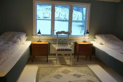 a bedroom with two beds and a chair and a window at Moonvalley Lodge - stort & koselig hus - Måndalen in Sæbø