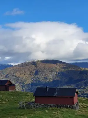 a barn on a hill with a mountain in the background at Molden 2-fjellutsikt og jacuzzi tilgang. in Luster