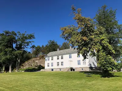 a large white building in a field with a tree at Storlauvøya The Atlantic Ocean Road in Karvåg