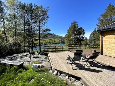 a man sitting in a chair on a deck with a dog at A cottage by the forest with a sea view ! in Søfstad