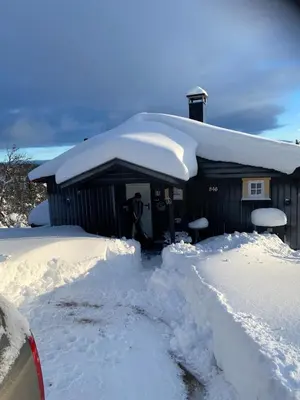 a house covered in snow with a man standing outside at Cabin in the Mountain, with Solar Energy in Slidre