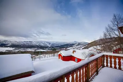 a snow covered balcony with a red house and mountains at Kvetos fjellgårdsutsikt in Beitostøl