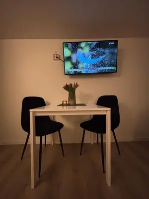 a dining room table with chairs and a tv on the wall at Litle cozy apartment in Ålesund in Ålesund