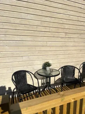 a table and four chairs on a deck with a wall at Cozy backyard apartment in Trondheim
