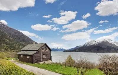 a wooden cabin on the side of a lake with mountains at Beautiful Home In Vallavik With Kitchen in Djønno