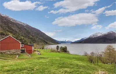 a red barn in a field next to a lake at Beautiful Home In Vallavik With Kitchen in Djønno