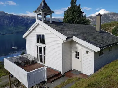 a small white church with a deck next to a lake at Spacious house by the Hardangerfjord in Hesthamar